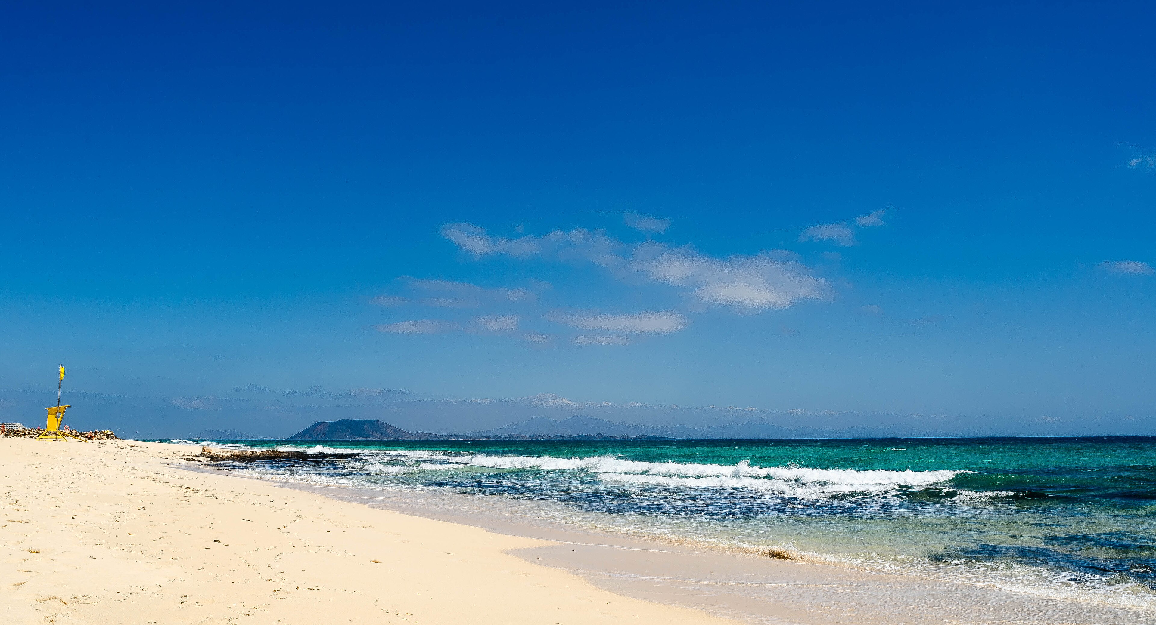 Playa de arena blanca y mar turquesa en Corralejo, Fuerteventura, con la isla de Lobos al fondo